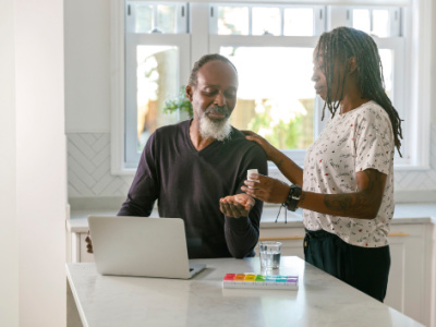 Black older man sitting in kitchen with young black woman helping him with medication