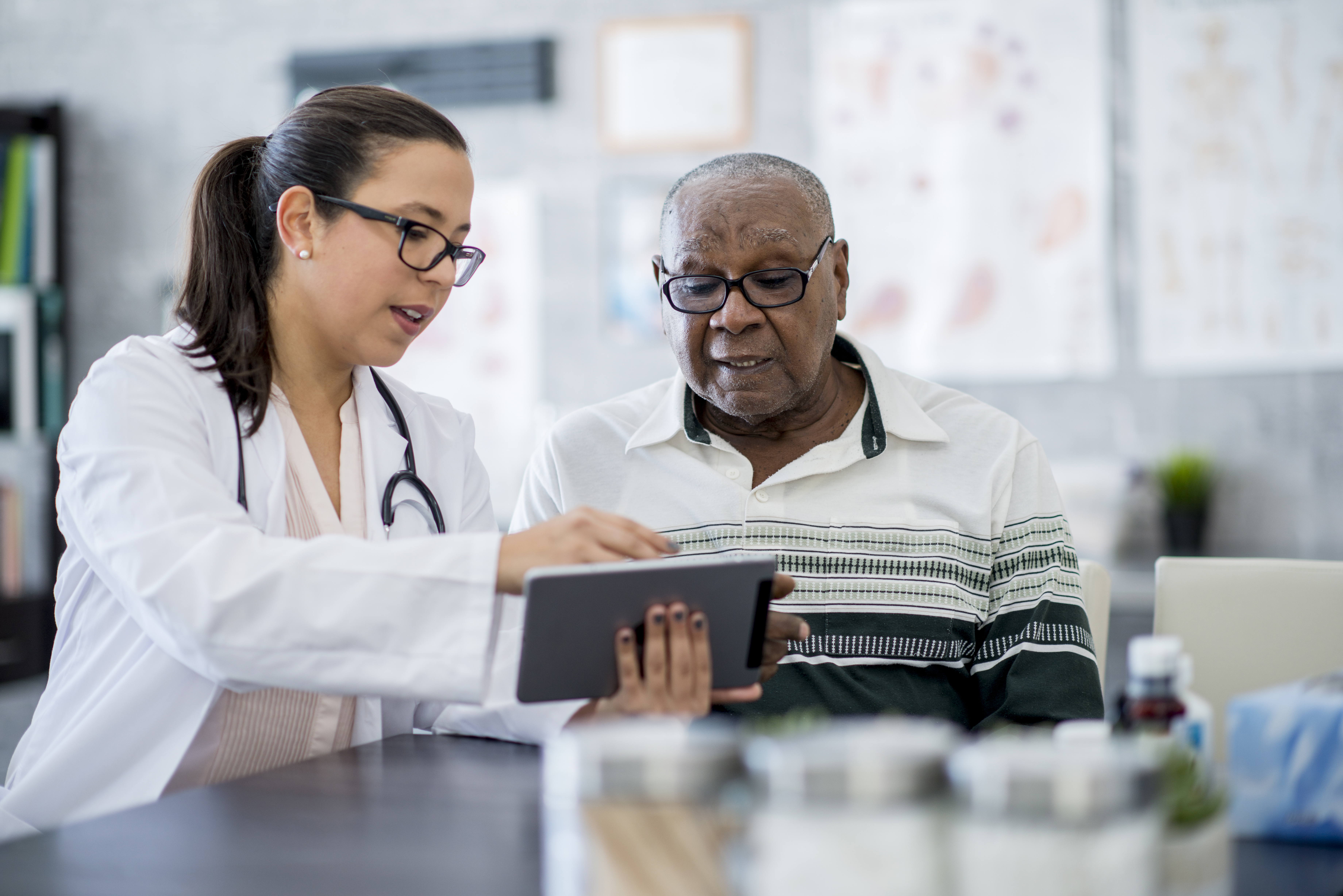 Female community health worker with elderly black man using tablet